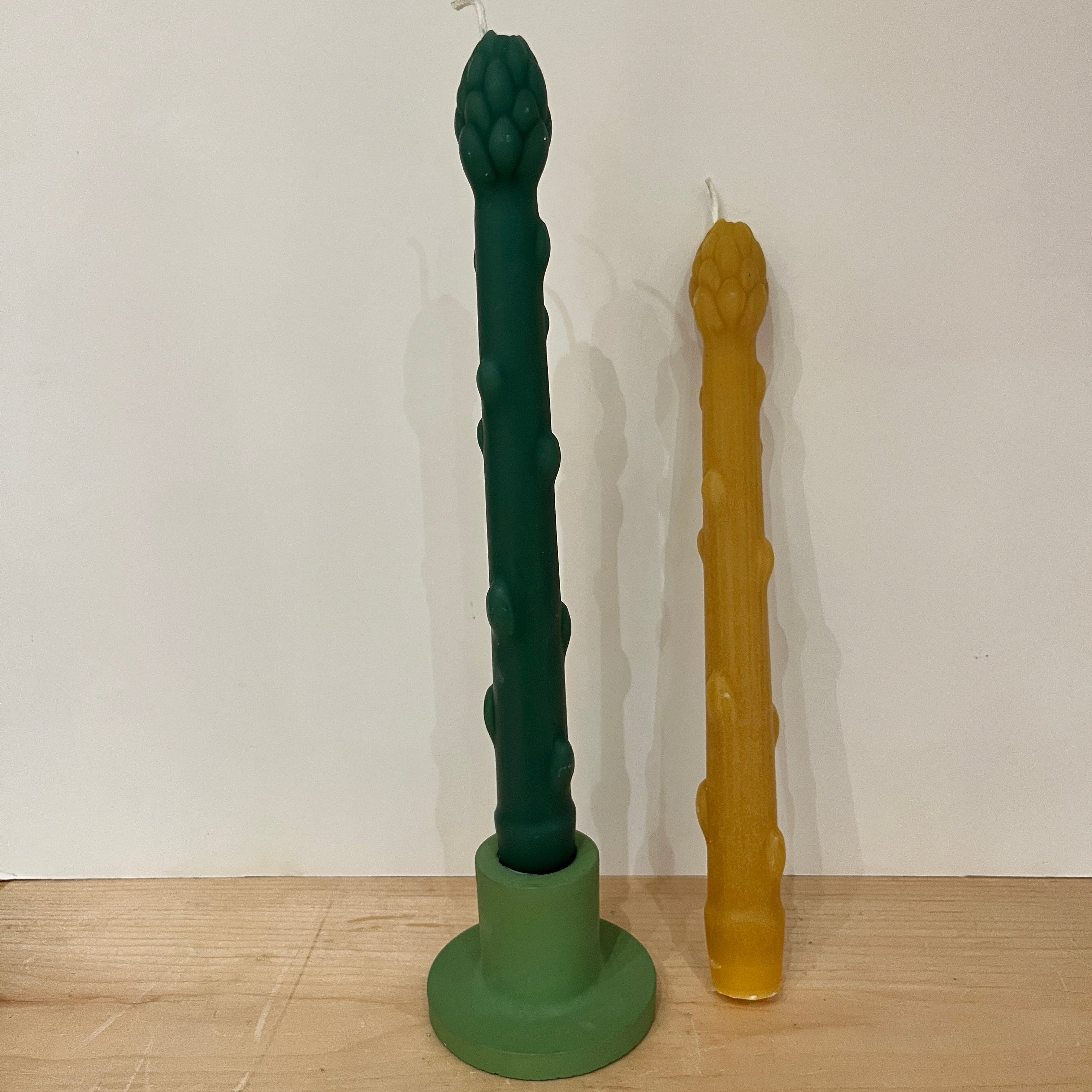 Two unique-shaped candles, one green and one brown, on a wooden surface with a white background.