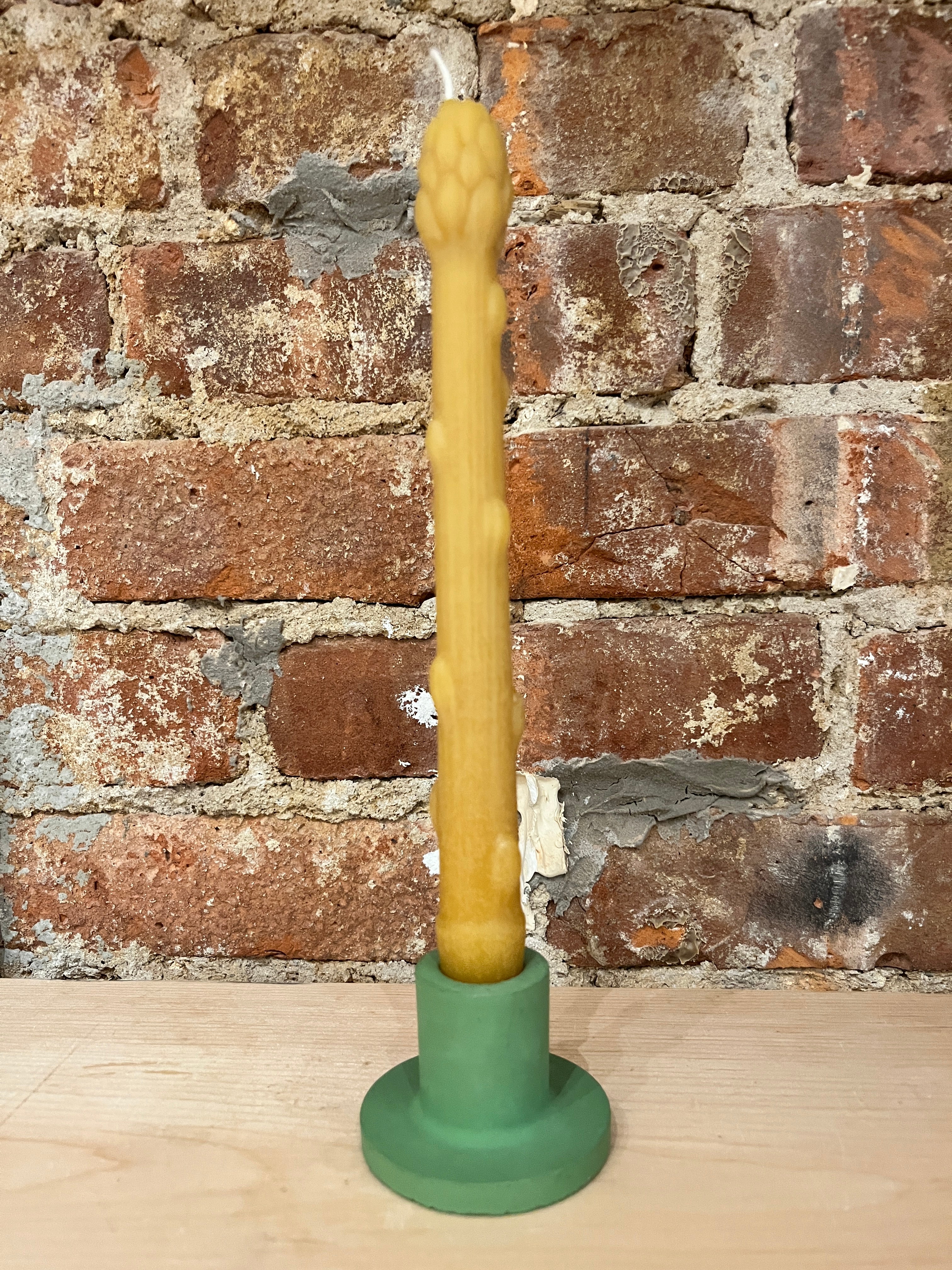Yellow candle in a green holder against a brick wall.