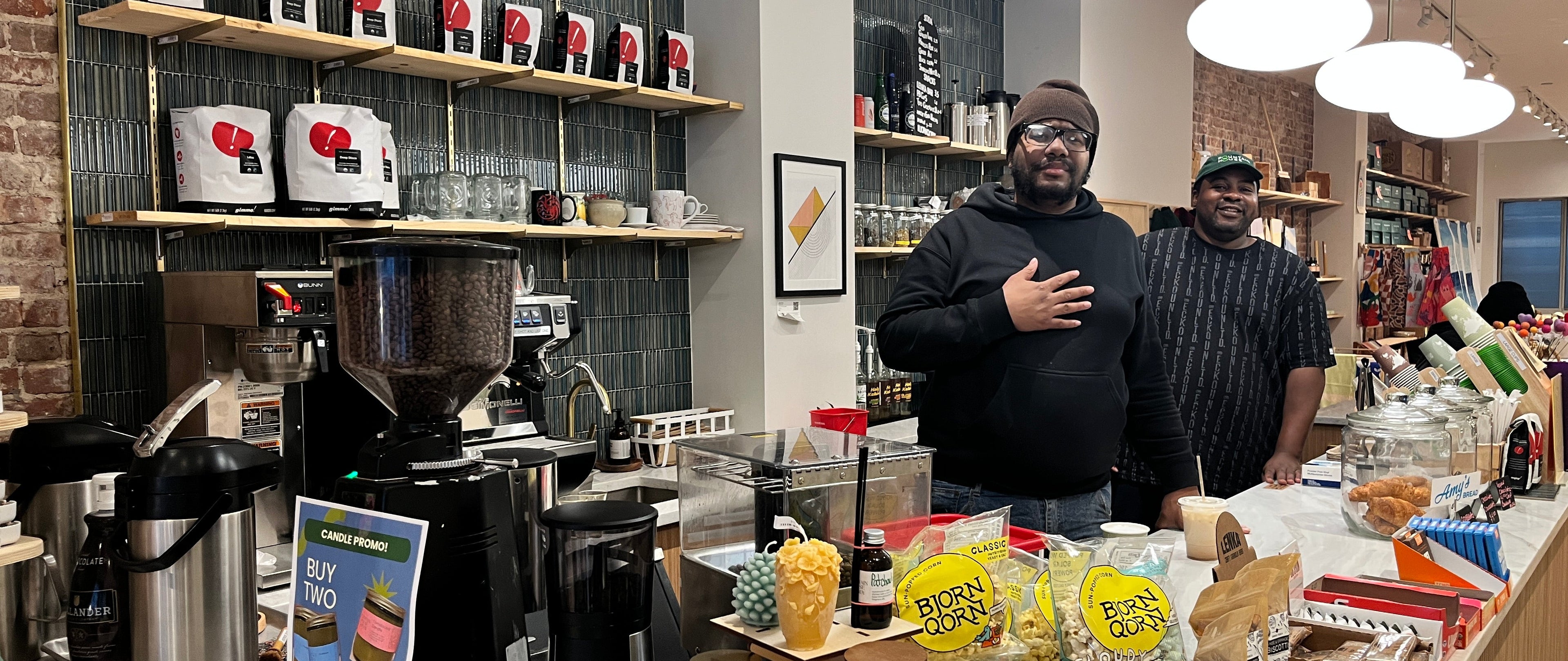 Two men standing in a coffee shop with shelves and counter displays.