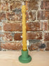 Yellow candle in a green holder against a brick wall.