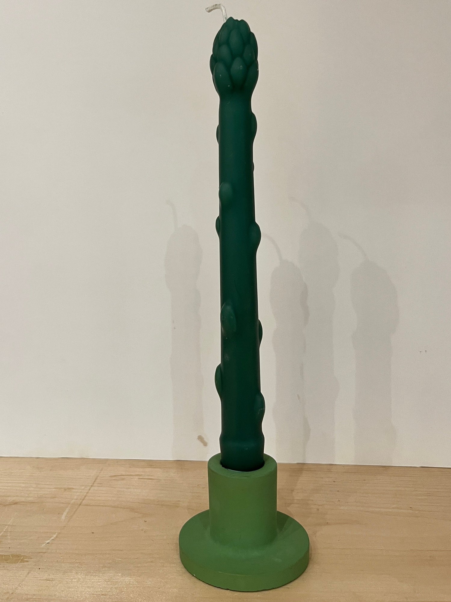 Green textured candle on a white wall background